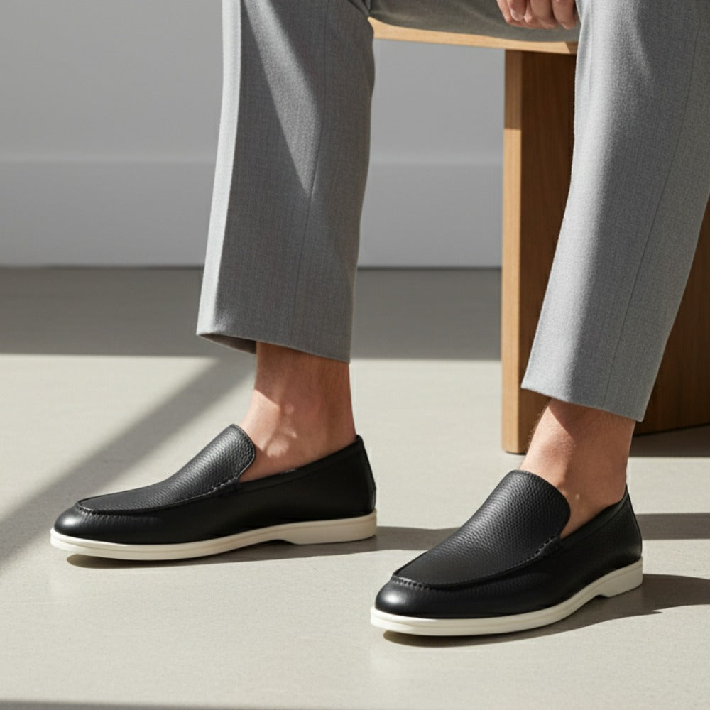 Black leather loafers by SanValier, with a textured finish and light-colored soles, styled with grey pants.