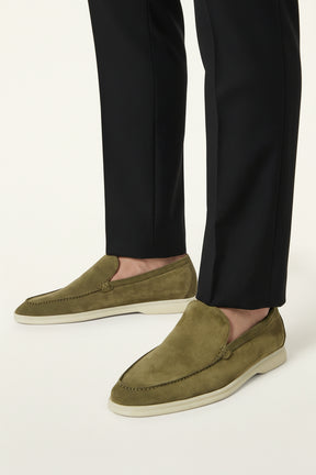 Green suede loafer by San Valier, styled with black trousers on a white background.