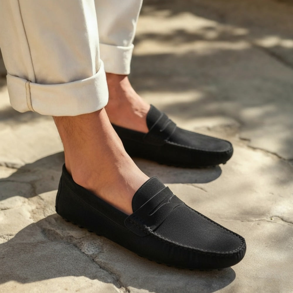 Black suede driver loafer by SanValier, with visible stitching, styled with rolled-up off-white pants.