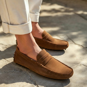 Men's brown suede driver loafer by San Valier, featuring moccasin-style stitching, and paired with cream-colored pants.